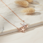 An asymmetrical rose gold starfish necklace featuring three coastal motifs, with a central pavé-set round stone design.