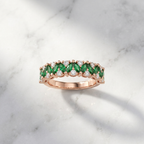 Studio flat lay of a rose gold emerald wedding band isolated cleanly on a smooth white stone surface.
