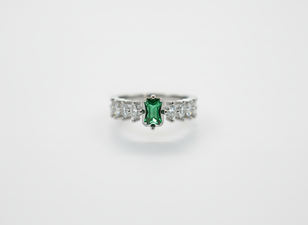 Macro photo of a forest green emerald ring focusing on the rectangular stone setting and round crystal side accents.