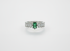 Macro photo of a forest green emerald ring focusing on the rectangular stone setting and round crystal side accents.