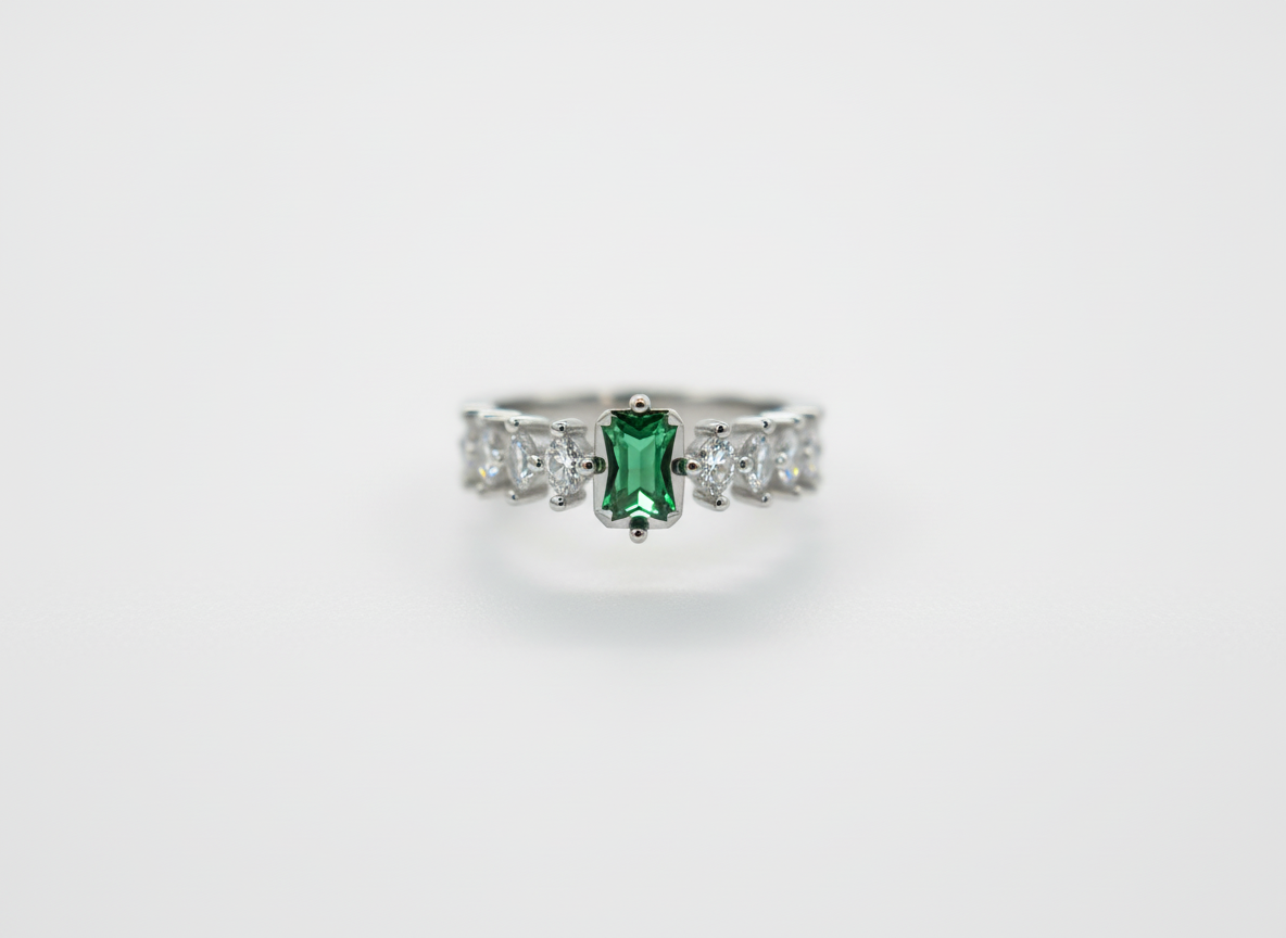 Macro photo of a forest green emerald ring focusing on the rectangular stone setting and round crystal side accents.