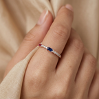 Close-up of a model wearing a slender ruby and sapphire ring in warm rose gold for a curated, modern aesthetic.