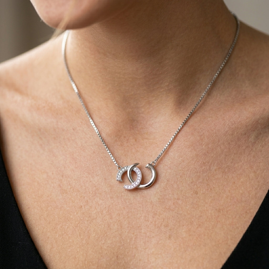 Silver necklace with a double crescent moon pendant on a person's neck.