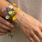 A polished silver heart charm bracelet acting as a foundation piece within a stacked layered jewelry look.