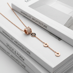 An elongated rose gold lariat necklace featuring a pavé-set cylinder and contrasting circular drop charms.