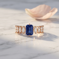 An emerald cut indigo sapphire ring in rose gold with brilliant marquise stones forming a winged architectural style.