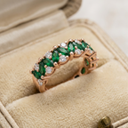Front view of a polished rose gold eternity band alternating marquise cut green emeralds and round diamonds.