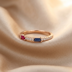 A premium multi-ring finger stack anchored by a sculptural rose gold ruby and sapphire ring with fine accent bands.