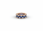 Studio flat lay of a sculptural rose gold band with deep blue stones on a smooth ceramic surface.