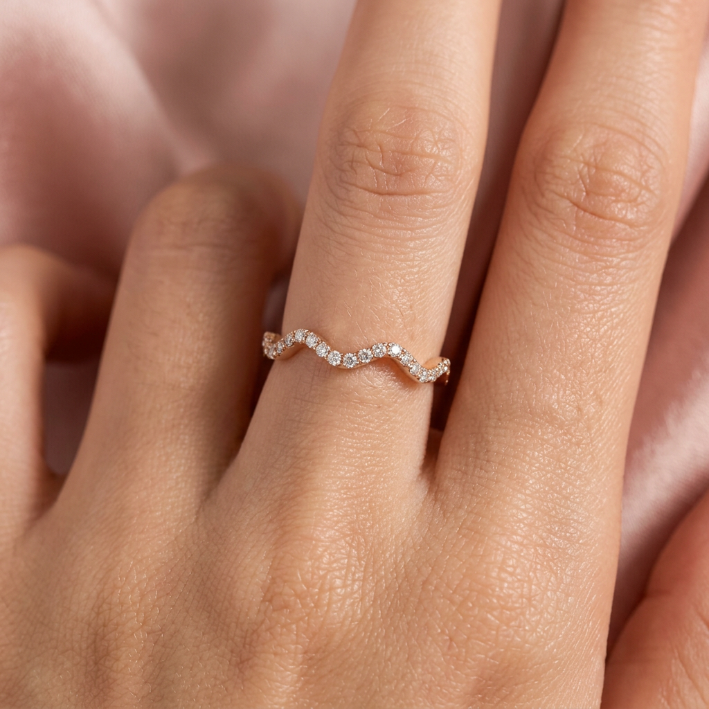 A curved pink gold wave ring stacked perfectly alongside a sleek minimalist band on a clean white surface.