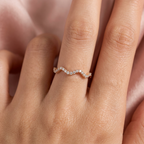 A curved pink gold wave ring stacked perfectly alongside a sleek minimalist band on a clean white surface.