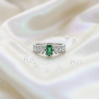 A forest green emerald ring with a rectangular stone flanked by alternating marquise and circular accents.