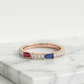 A slender rose gold ruby and sapphire ring featuring sharp baguette gemstones framed by brilliant round pavé diamonds.