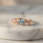 Modern rose gold heart ring featuring a cerulean blue stone accented by a cluster of lab grown diamonds.