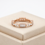 A rose gold eternity ring featuring an alternating textured pattern of baguette cut stones and round white seed pearls.