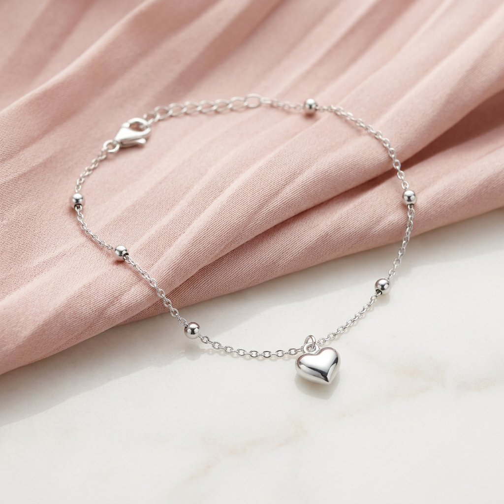 High-polish silver chain bracelet featuring structural beads and a central puffed heart charm pendant.