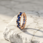An elegant rose gold eternity ring with navy marquise stones, styled for modern evening attire.